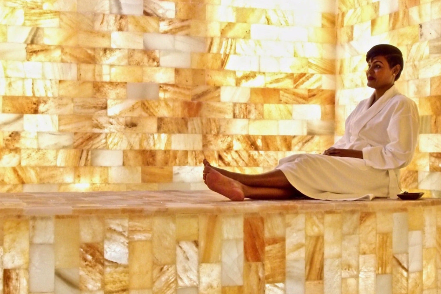 Guest seated on a salt bench inside an illuminated Himalayan salt room